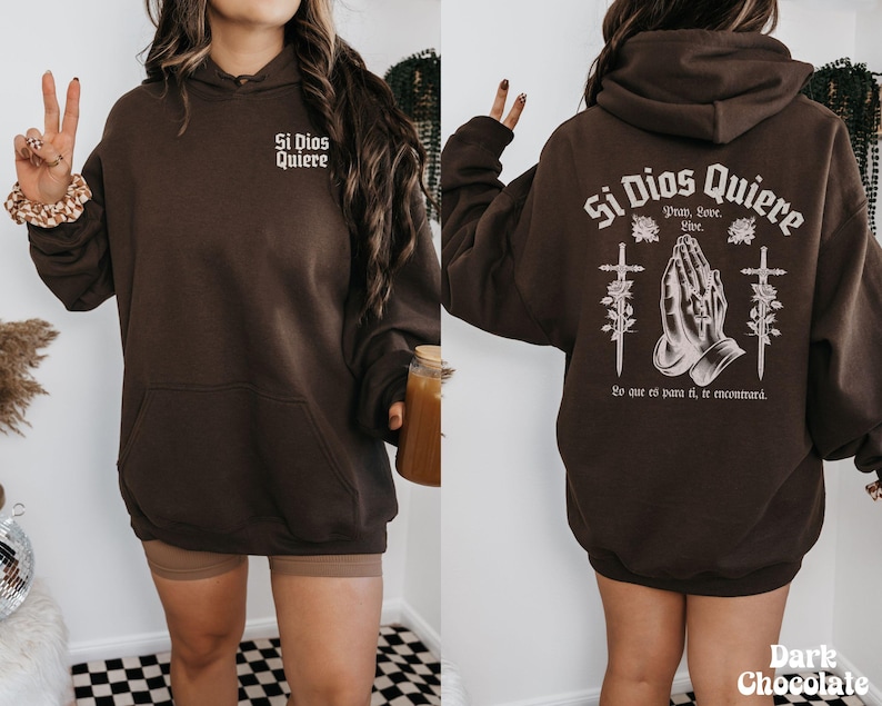 May include: A brown hoodie with the text "Si Dios Quiere" in white lettering. The text is surrounded by a graphic of two hands in prayer with crosses and flowers. The text "Pray, Love, Live" is below the hands. The text "Lo que es para ti, te encontrar&aacute;" is below the graphic.