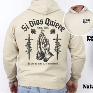 May include: A beige hoodie with a black print on the back that says "Si Dios Quiere" with a praying hands design and two swords. The front of the hoodie has a smaller print that says "Si Dios Quiere".