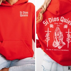 May include: Red hooded sweatshirt with the text "Si Dios Quiere" on the front and back. The back design includes praying hands, swords, and roses. The text on the back also includes "Pray, Love, Live" and "Lo que es para ti, te encontrar&aacute;."