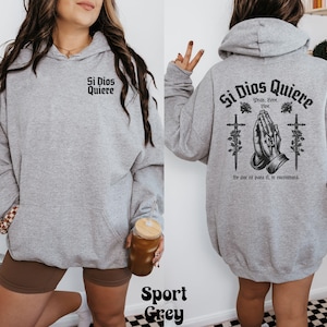 May include: A gray hooded sweatshirt with the text "Si Dios Quiere" and a graphic of praying hands with crosses. The text below the graphic reads "Pray, Love, Live.  Se que es para ti, si te encuentras."