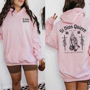 May include: Light pink hoodie with a graphic print of praying hands and the text "Si Dios Quiere" in black. The text below the graphic says "Pran, Love, Live" and "Yo que to para ti, te encontrar&aacute;".