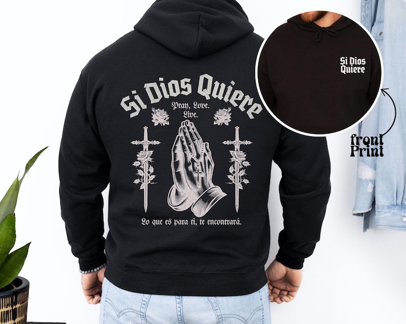 May include: Black hooded sweatshirt with a white print on the back that says "Si Dios Quiere" with a graphic of praying hands and two swords. The front of the sweatshirt has a smaller white print that says "Si Dios Quiere".
