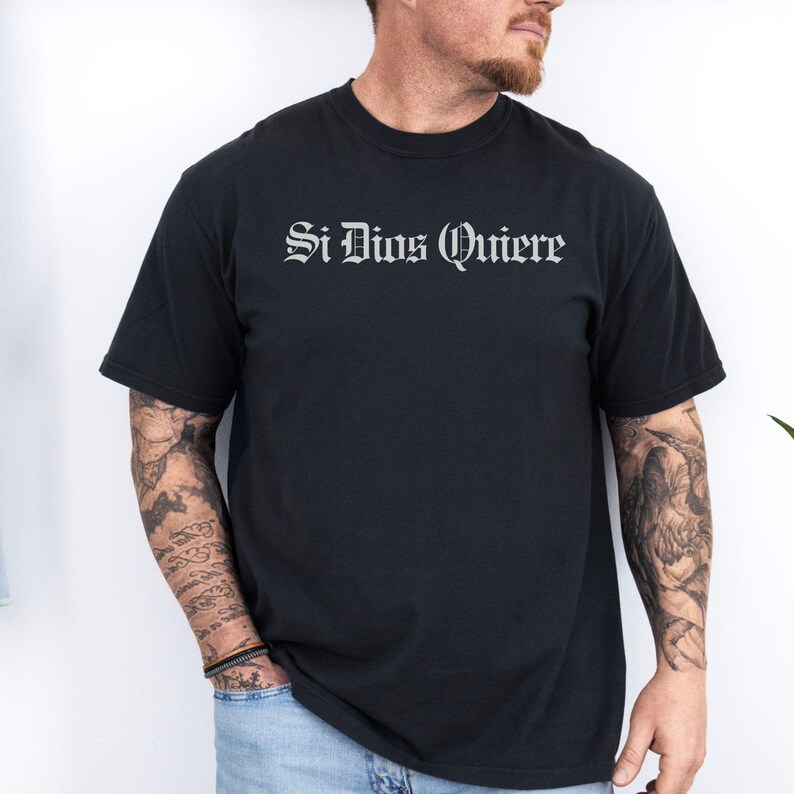 Si Dios Quiere” in Old English font on a Comfort Colors tee. Spanish for “if God wills it.” A humble, faith-filled expression often used in prayer, hope, and daily life. Soft vintage wash cotton.