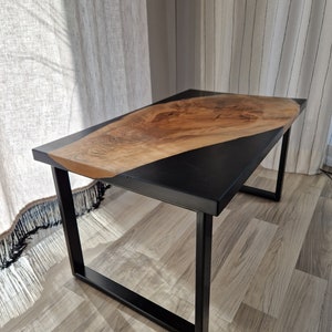 Könnte beinhalten: Ein schwarzer Metalltisch mit einer Holzplatte. Die Platte ist aus Naturholz mit einer schwarzen Epoxidharzfüllung. Der Tisch hat ein schlichtes, modernes Design.