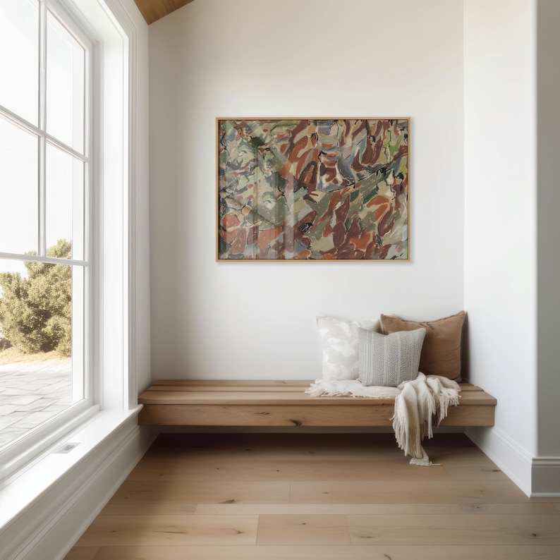 May include: A modern interior scene featuring a wooden bench with pillows and a blanket beneath an abstract painting in a wooden frame. The room has a large window and light-colored hardwood flooring.