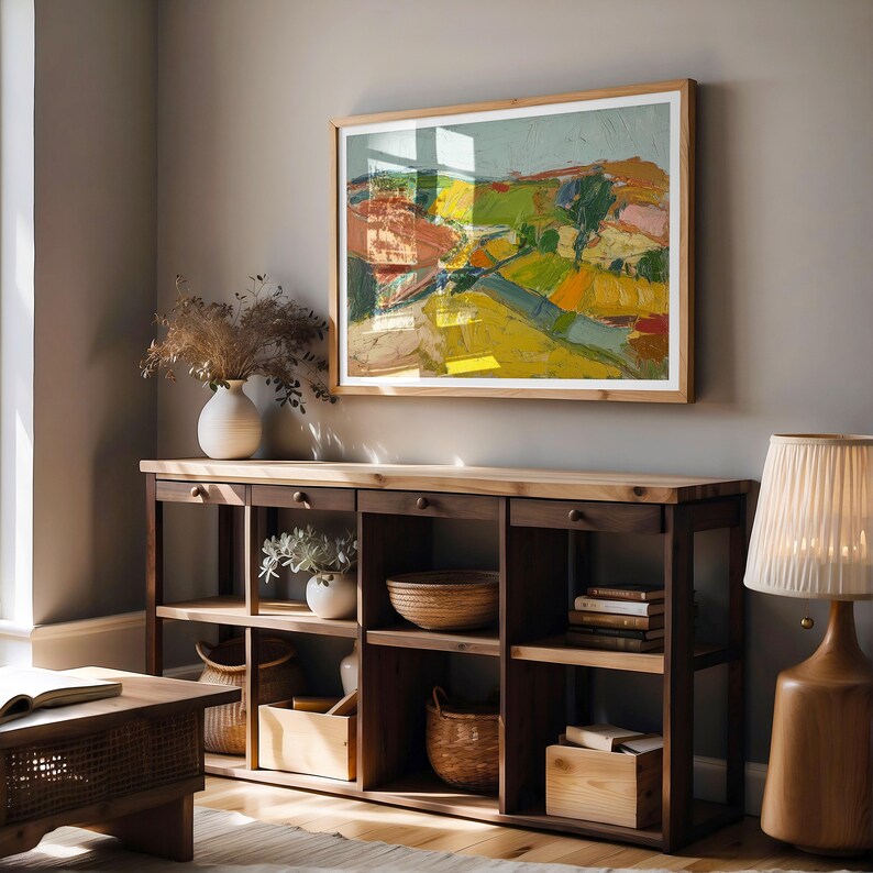 以下が含まれることがあります： 木製のフレームに入った抽象的な風景画が、木製のコンソールテーブルの上に飾られています。絵画は、黄色、緑、赤などの鮮やかな色を使用しています。コンソールテーブルには、花瓶やバスケットなどの装飾品が置かれたオープンシェルフと引き出しがあります。