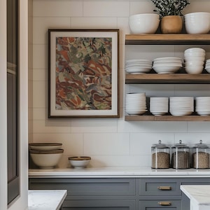 May include: A kitchen scene featuring a framed abstract painting with brown and green tones. Open wooden shelves display white bowls and plates. Gray cabinets with gold hardware and glass jars with grains complete the modern kitchen design.