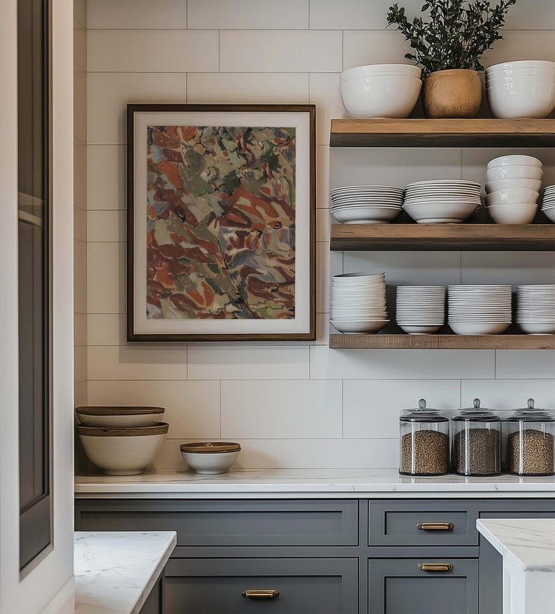 May include: A kitchen scene featuring a framed abstract painting with brown and green tones. Open wooden shelves display white bowls and plates. Gray cabinets with gold hardware and glass jars with grains complete the modern kitchen design.