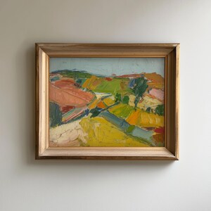 以下が含まれることがあります： 木製のフレームに入った抽象的な風景画。黄色、緑、ピンク、青など、鮮やかな色彩が使用され、筆致がはっきりと見て取れます。絵はなだらかな丘と明るい空を描いています。