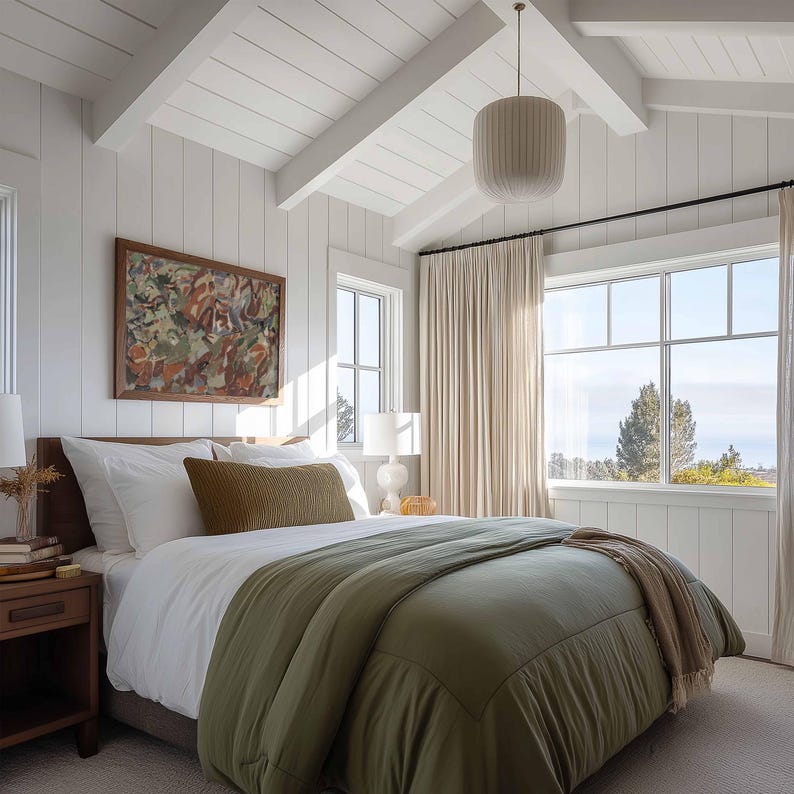 May include: A bedroom with white walls, ceiling, and trim. A bed with white linens, an olive green comforter, and a brown headboard. A framed abstract painting hangs above the bed. A large window with beige curtains and a pendant light.