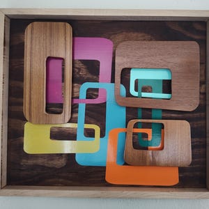 Pode incluir: Arte de parede abstrata com um design geométrico com quadrados sobrepostos em várias cores, incluindo amarelo, laranja, turquesa, verde e rosa. Os quadrados são feitos de madeira e têm um acabamento de grão de madeira natural.
