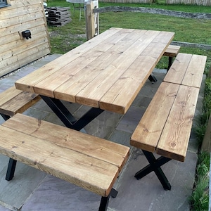 May include: A wooden picnic table with two matching benches. The table and benches are made of light-coloured wood with visible grain. The table and benches have black metal legs. The table is approximately 183 cm long and 91 cm wide.