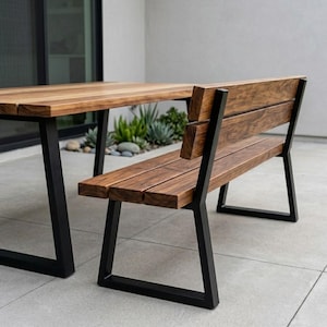 May include: A contemporary wooden bench and table set. The bench and table feature a dark wood finish and black metal legs. The bench has a backrest, and the table is rectangular. The set is positioned outdoors on a concrete patio.