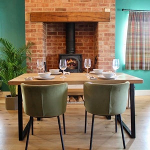 May include: A dining room table with four chairs and a wooden top. The table is set with plates, cutlery, and glasses. There is a fireplace in the background with a wood-burning stove.