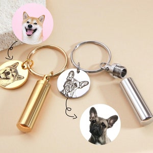 Puede incluir: Dos llaveros plateados con un pequeño cilindro adjunto. Cada llavero tiene un dije redondo con una foto en blanco y negro de la cara de un perro. Un dije tiene un Shiba Inu y el otro tiene un Bulldog Francés.