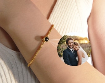 May include: A gold bracelet with a black gemstone charm. The charm has a small photo of a couple inside.