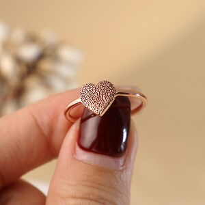 May include: A rose gold ring featuring a heart-shaped design. The heart has a textured pattern.