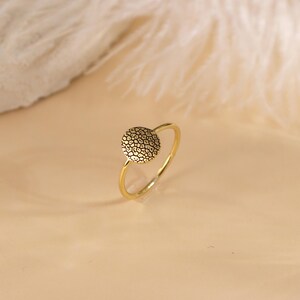 May include: A gold ring featuring a textured round design. The ring is simple and delicate.