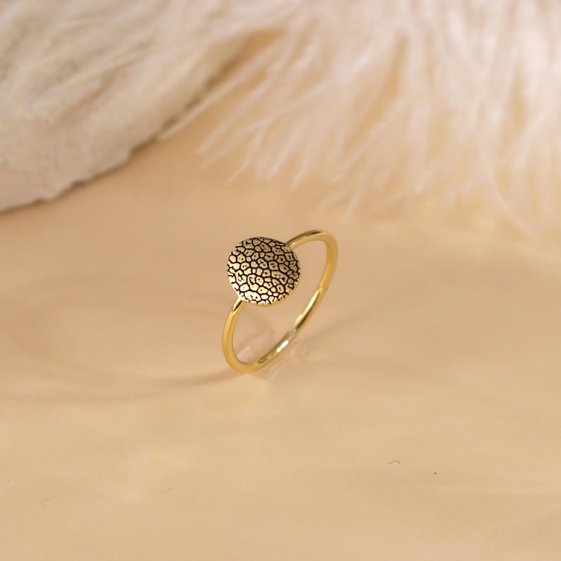 May include: A gold ring featuring a textured round design. The ring is simple and delicate.