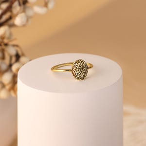 May include: A gold ring with a textured round design. The ring is on a white surface.