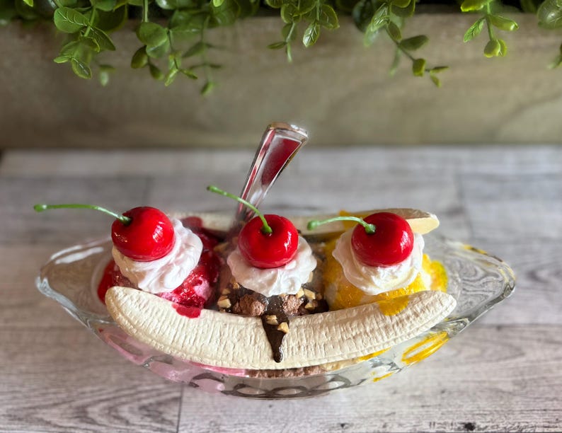 Pu&ograve; includere: Un banana split sundae con tre palle di gelato, guarnito con panna montata, ciliegie e salsa al cioccolato. Il sundae viene servito in una ciotola di vetro con una banana in cima.