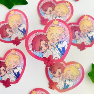 May include: A set of heart-shaped stickers featuring two cartoon characters. The characters are a blonde boy with a crown and a red-haired boy with a bow tie. The stickers are pink and white with a glittery finish.