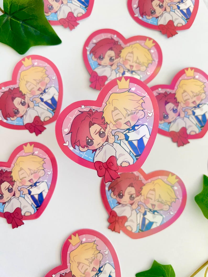 May include: A set of heart-shaped stickers featuring two cartoon characters. The characters are a blonde boy with a crown and a red-haired boy with a bow tie. The stickers are pink and white with a glittery finish.