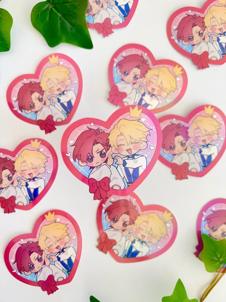May include: A set of 10 heart-shaped stickers featuring two cartoon characters. The characters are a blonde-haired person with a crown and a red-haired person. The stickers are pink and white with a glittery finish.