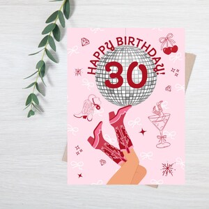 Puede incluir: Tarjeta de cumplea&ntilde;os rosa con el texto "HAPPY BIRTHDAY! 30" encima de una bola de discoteca. La tarjeta presenta ilustraciones de botas de vaquero, un c&oacute;ctel y otros elementos decorativos. La tarjeta est&aacute; sobre una superficie de madera blanca.