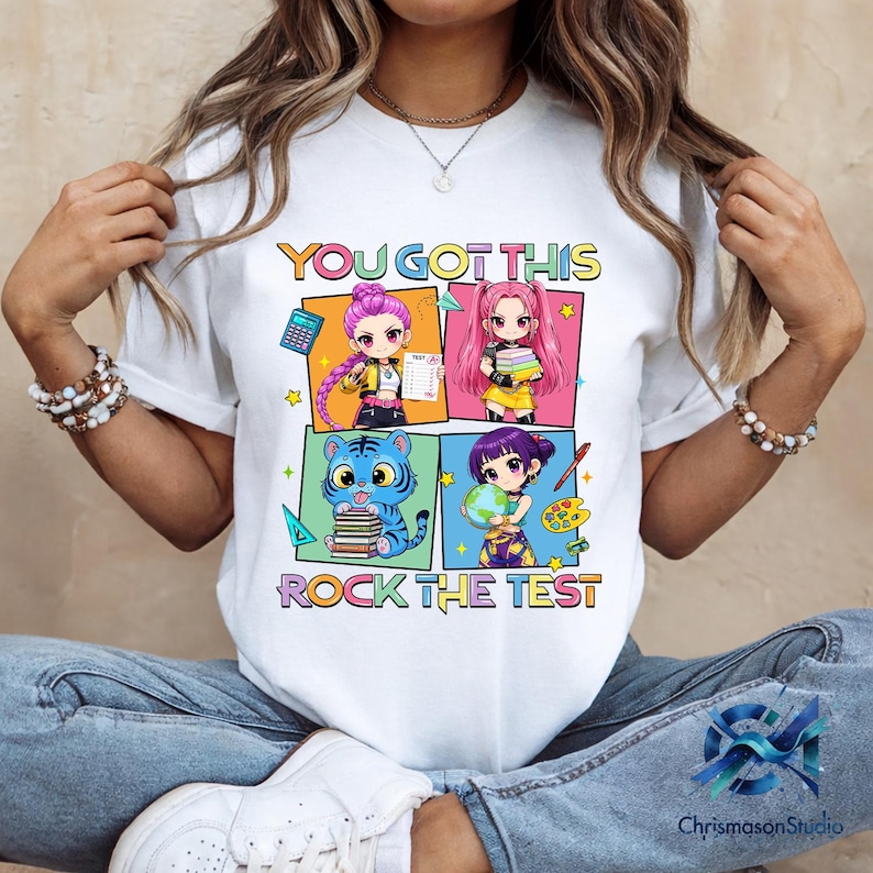 May include: White t-shirt with a colorful graphic that says "YOU GOT THIS ROCK THE TEST". The graphic features four anime-style characters and a tiger holding books. The shirt is worn by a person.