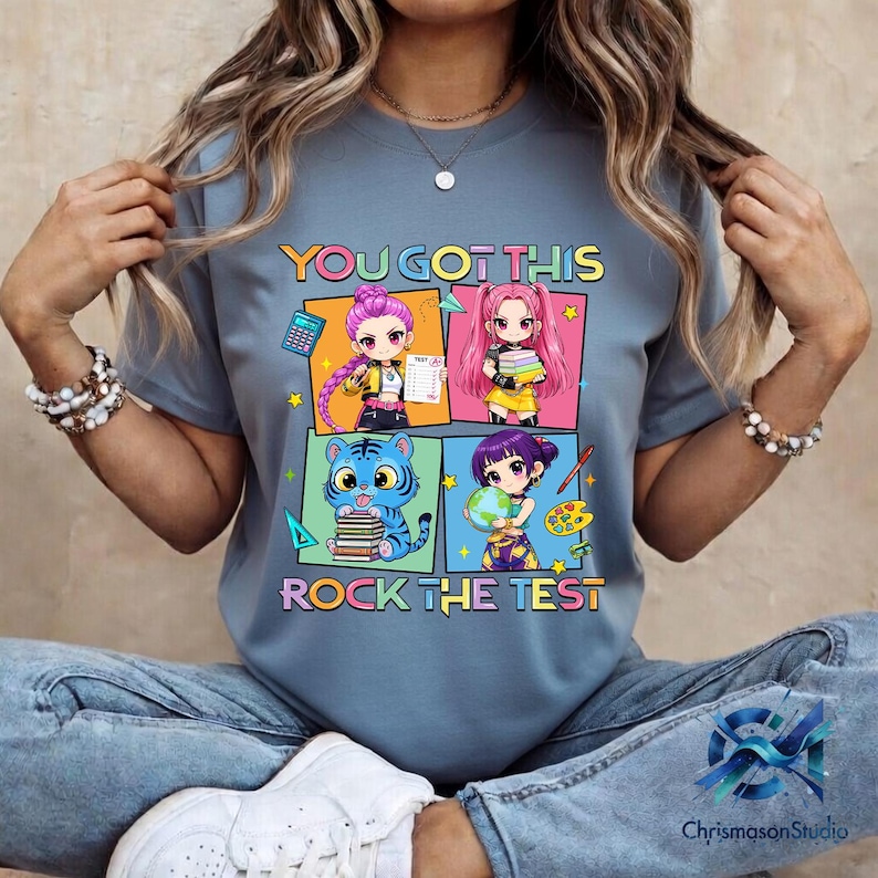 May include: A blue t-shirt with the text "YOU GOT THIS ROCK THE TEST" and a colorful graphic featuring four anime-style characters. The graphic includes a calculator, books, a globe, and paint supplies.