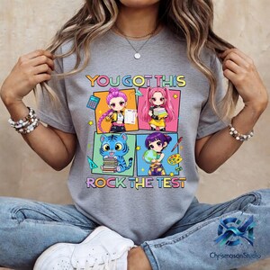 May include: Gray t-shirt with the text "YOU GOT THIS ROCK THE TEST" and colorful anime-style illustrations. The design features four panels with characters holding school-related items like books, a calculator, and a globe.