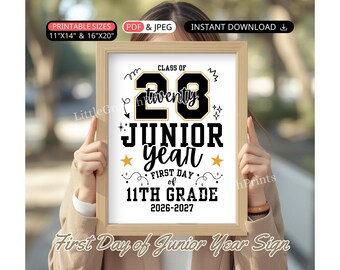 May include: A rectangular wooden frame containing a white sign with black and gold text that reads Class of 28, twenty, Junior Year, First Day of 11th Grade, and 2026-2027. The design includes decorative stars, swirls, and sparkles on a white background.
