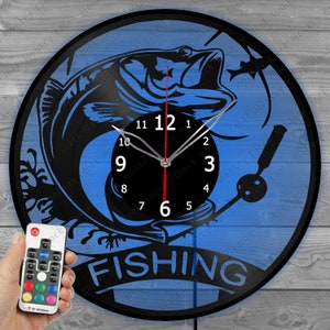 May include: A blue and black vinyl record clock with a silhouette of a fish jumping out of the water. The clock face has black numbers and hands. The words "FISHING" are printed in black below the clock face. The clock is illuminated with colorful LED lights.