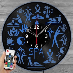 May include: A black vinyl record clock with a blue and white design featuring various spa and wellness symbols. The clock face has a white background with black numbers and hands. The clock is illuminated with a multi-colored LED light and comes with a remote control.
