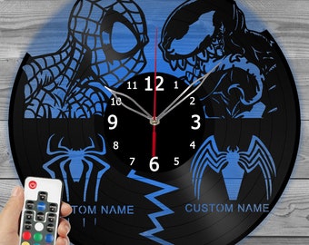 Könnte beinhalten: Eine schwarze Vinyl-Schallplattenuhr mit blauen Silhouetten von Spider-Man und Venom. Die Uhr hat einen roten Sekundenzeiger und eine Fernbedienung. Das Design der Uhr enthält den Text "CUSTOM NAME".
