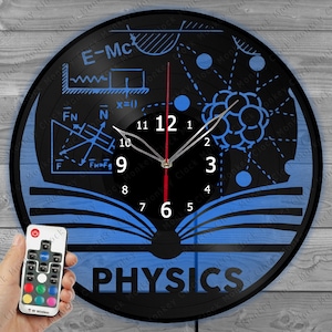 May include: A black vinyl record clock with a blue and white design featuring physics formulas and a book. The clock has a white face with black numbers and hands. The clock is illuminated with a blue light and has a remote control.