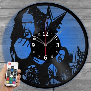 May include: A black vinyl record clock with a blue background. The clock features a band silhouette design and a black clock face with white numbers and hands. A remote control is visible.