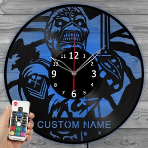 May include: Black vinyl record clock with a blue background featuring a skull graphic and the text "CUSTOM NAME". The clock has white numbers and hands, and a red second hand. A remote control is in the image.