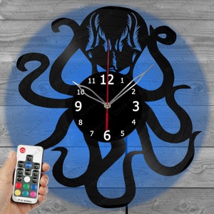 Könnte beinhalten: Eine schwarze Schallplattenuhr in Form eines Kraken mit einem roten Sekundenzeiger. Die Uhr verfügt über eine Fernbedienung mit mehreren Farboptionen.