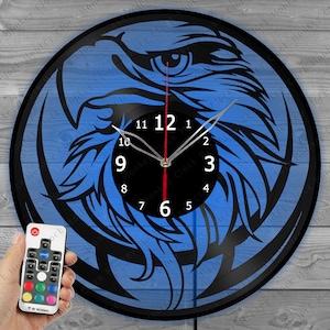 Könnte beinhalten: Eine blaue und schwarze Vinyl-Plattenuhr mit einem Adler-Design. Die Uhr hat ein schwarzes Zifferblatt mit weißen Zahlen und Zeigern. Die Uhr wird mit einem blauen Licht beleuchtet. Die Uhr wird mit einer Fernbedienung geliefert.