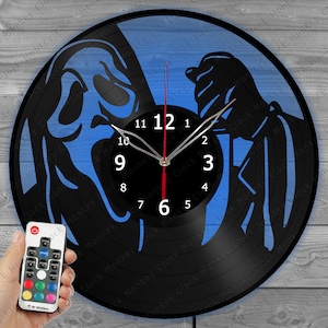 Puede incluir: Un reloj de vinilo negro con fondo azul que presenta una silueta de dos figuras de la película Scream. El reloj tiene una aguja de segundos roja y una aguja de minutos y horas blanca. El reloj está iluminado con luces LED y viene con un control remoto.