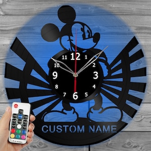 May include: A black vinyl record clock featuring a silhouette of Mickey Mouse with a blue background. The clock has a black and white design with a red second hand. The clock has a remote control with multiple color options. The clock has a space for a custom name.