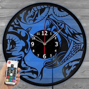 May include: A black and blue decorative wall clock with a snake design. The clock face is black with white numbers and hands. The clock is made from a vinyl record and includes a remote control.