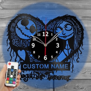 May include: A black and white vinyl record clock featuring a silhouette of Jack Skellington and Sally from the Nightmare Before Christmas movie. The clock has a blue background and a red heart shape. The clock face is black with white numbers and hands. The clock has a remote control with multiple color options. The text "CUSTOM NAME" and "Together Forever" is printed on the clock.