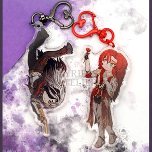 May include: Two anime-style character charms with red heart-shaped keychains. The charm on the left is a black-haired character with a gun, and the charm on the right is a red-haired character holding a red rose.