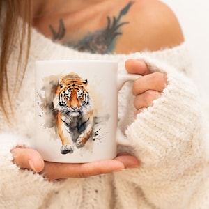 Op de afbeelding: Witte keramische mok met een aquarel-illustratie van een tijger die naar de kijker loopt. De tijger heeft oranje en zwarte strepen op een witte achtergrond.