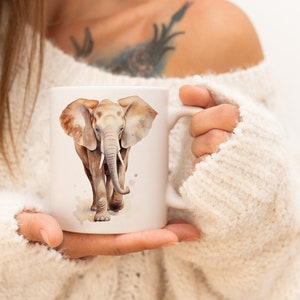 Op de afbeelding: Witte keramische mok met een aquarel-illustratie van een olifant. De olifant is bruin en grijs met grote oren en een slurf.