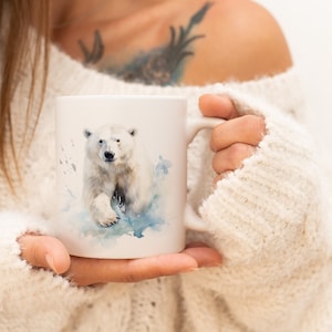 Könnte beinhalten: Weiße Keramiktasse mit einer Aquarell-Illustration eines Eisbären, der auf Eis geht. Der Bär ist nach vorne gerichtet und hat einen hellblauen Hintergrund.