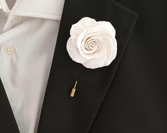 May include: A white rose boutonniere with a gold pin. The rose is made of fabric and has a realistic appearance.
